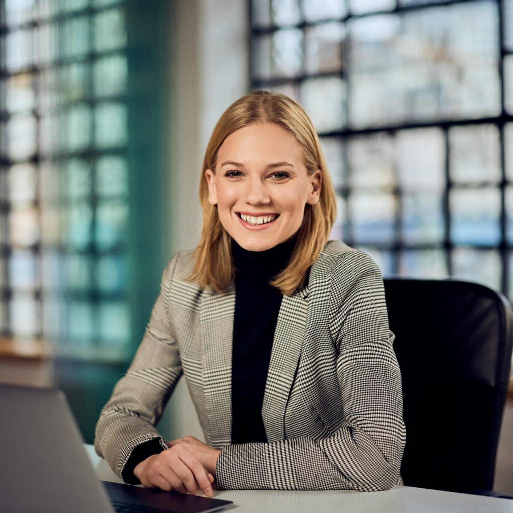 confident businesswoman smiling at office desk with laptop on modern workspace