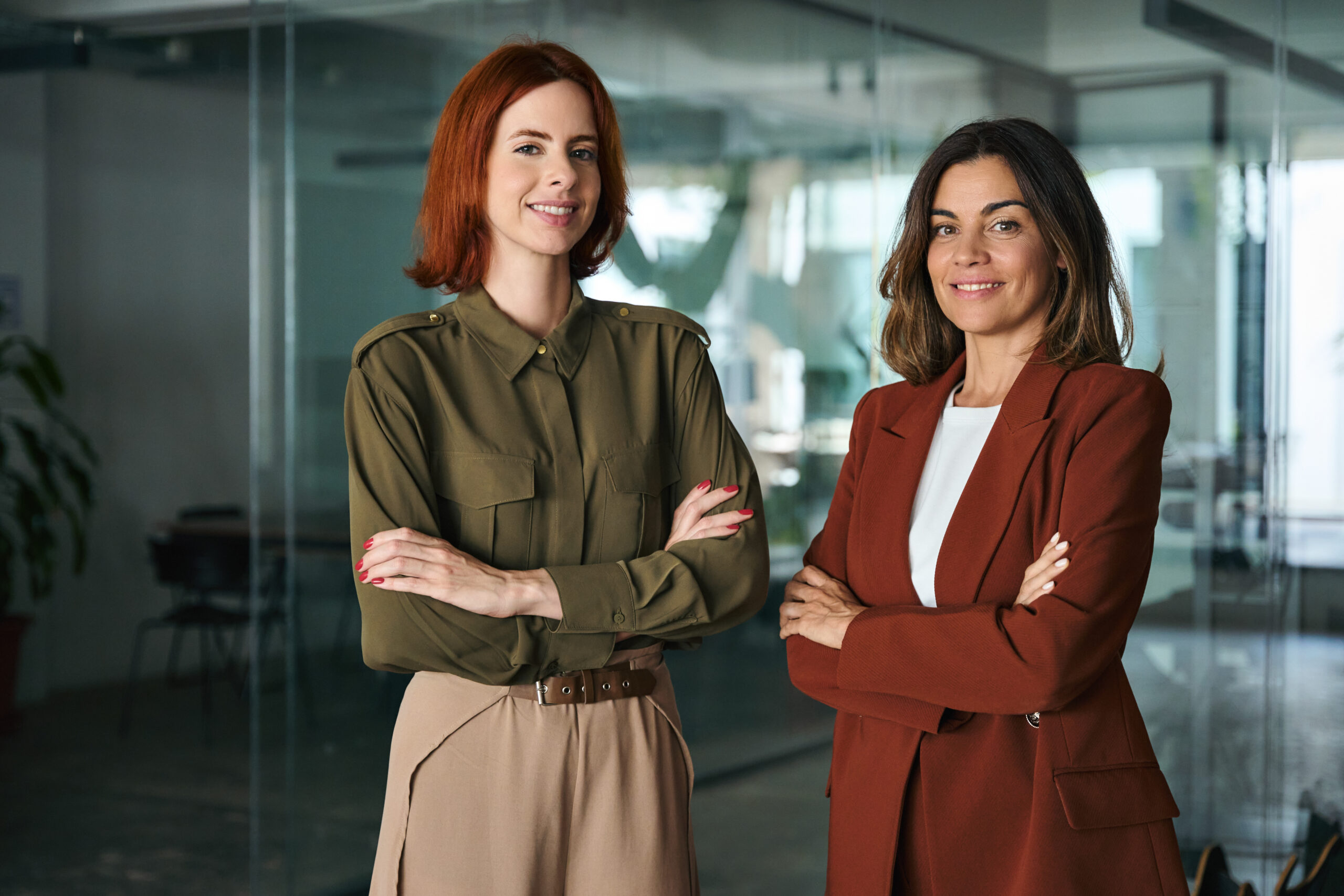 two smiling confident business women standing arms crossed in office, portrait.